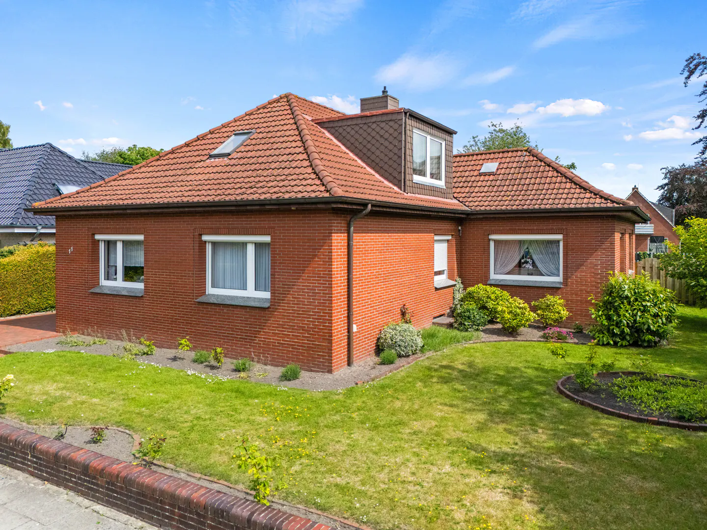 A red brick house with a tiled roof, white-framed windows, and a well-maintained lawn under a bright blue sky.
