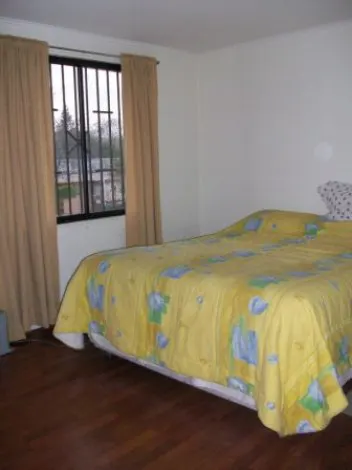 Bedroom with a yellow floral bedspread, hardwood floors, and a window with beige curtains.