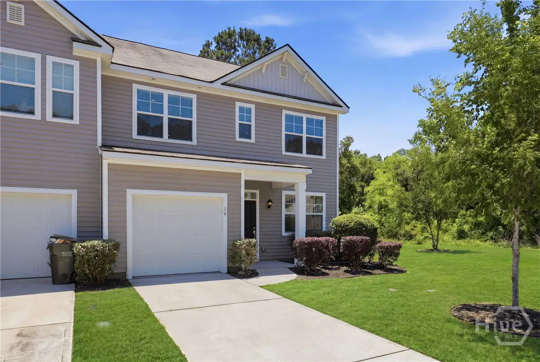 Two-story gray townhouse with white garage door, black front door, and green lawn under a blue sky.