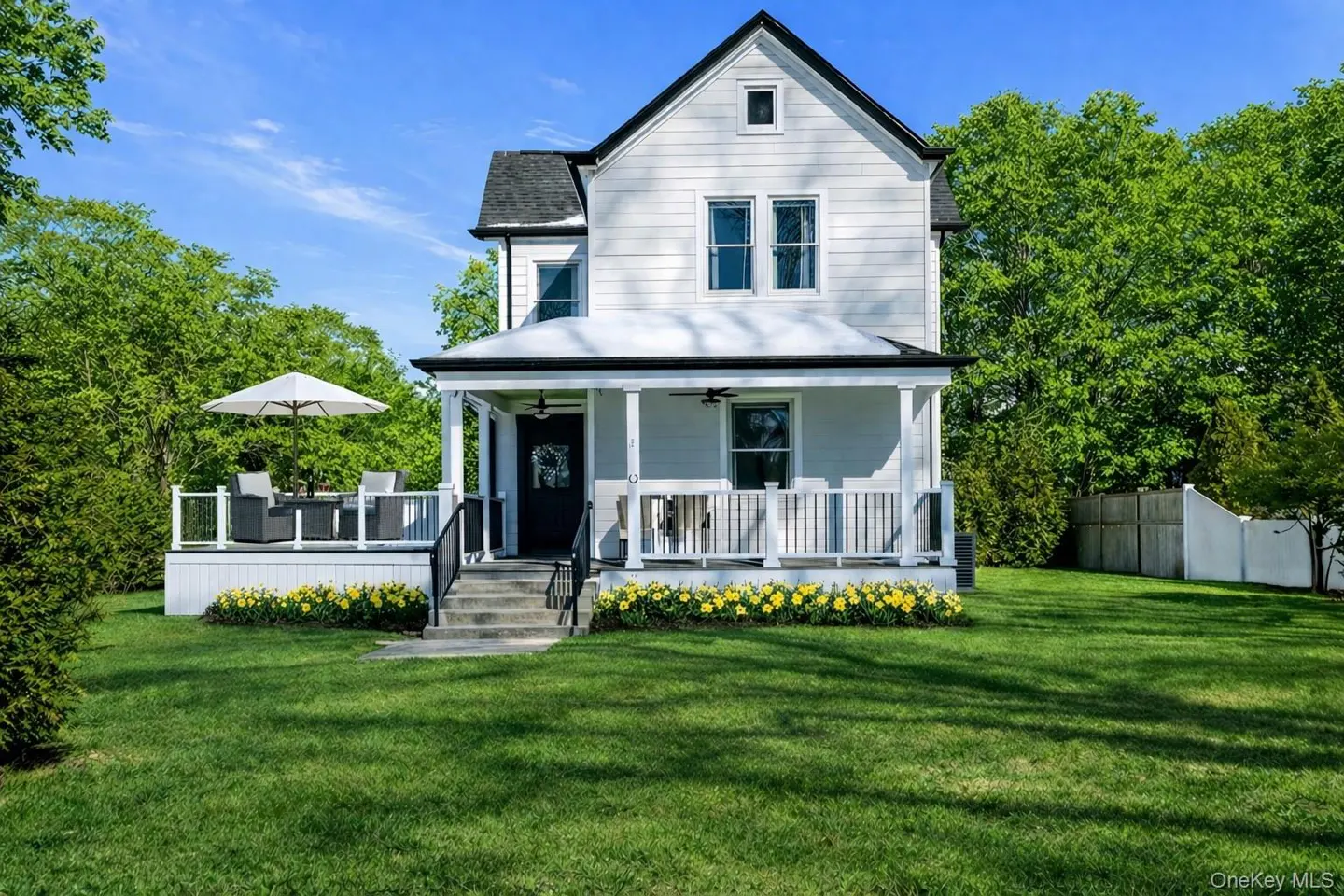 Two-story white house with a black roof, a porch, and a green lawn on a sunny day.
