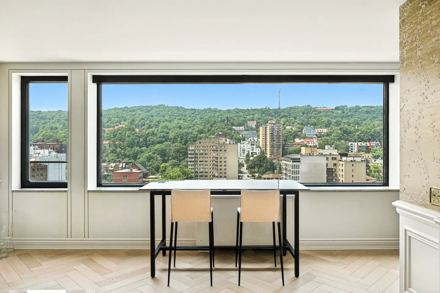 Interior view of a room with a table and chairs facing a large window with a city view.