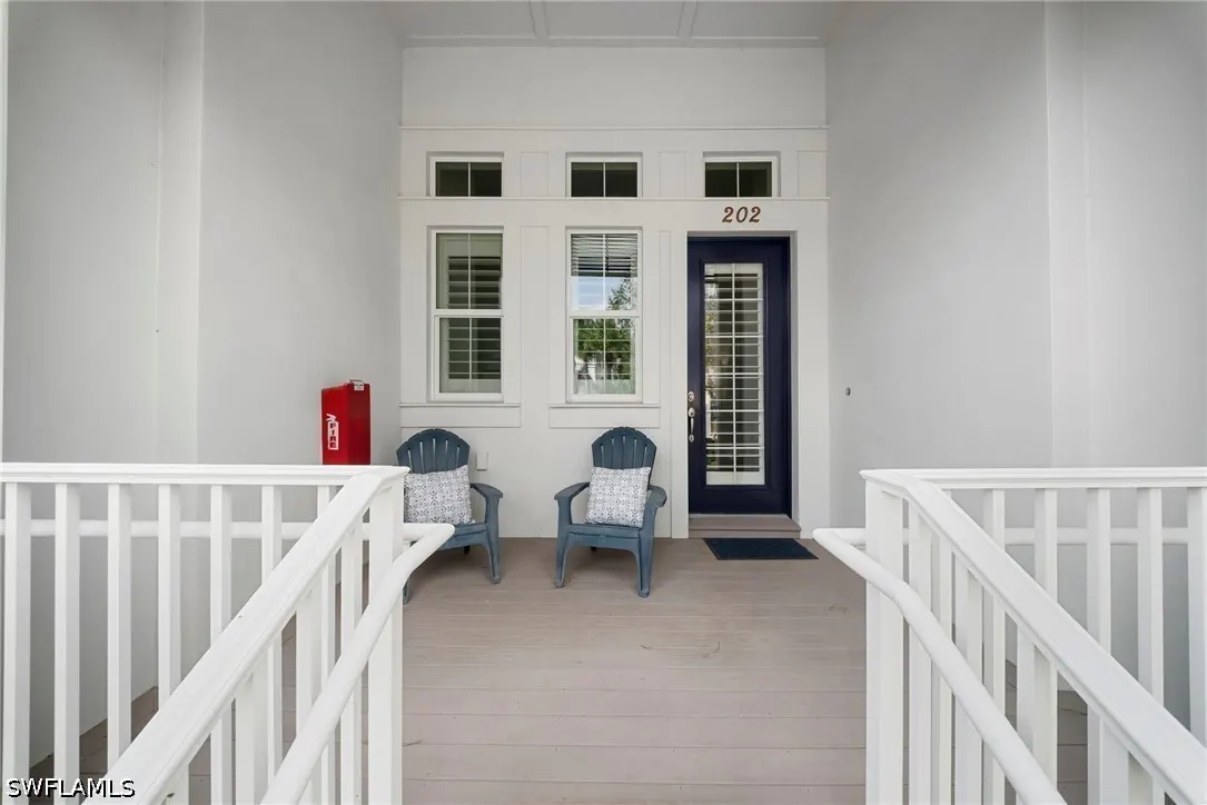 Front porch view of unit 202 with blue chairs, white railings, and a red fire extinguisher box.