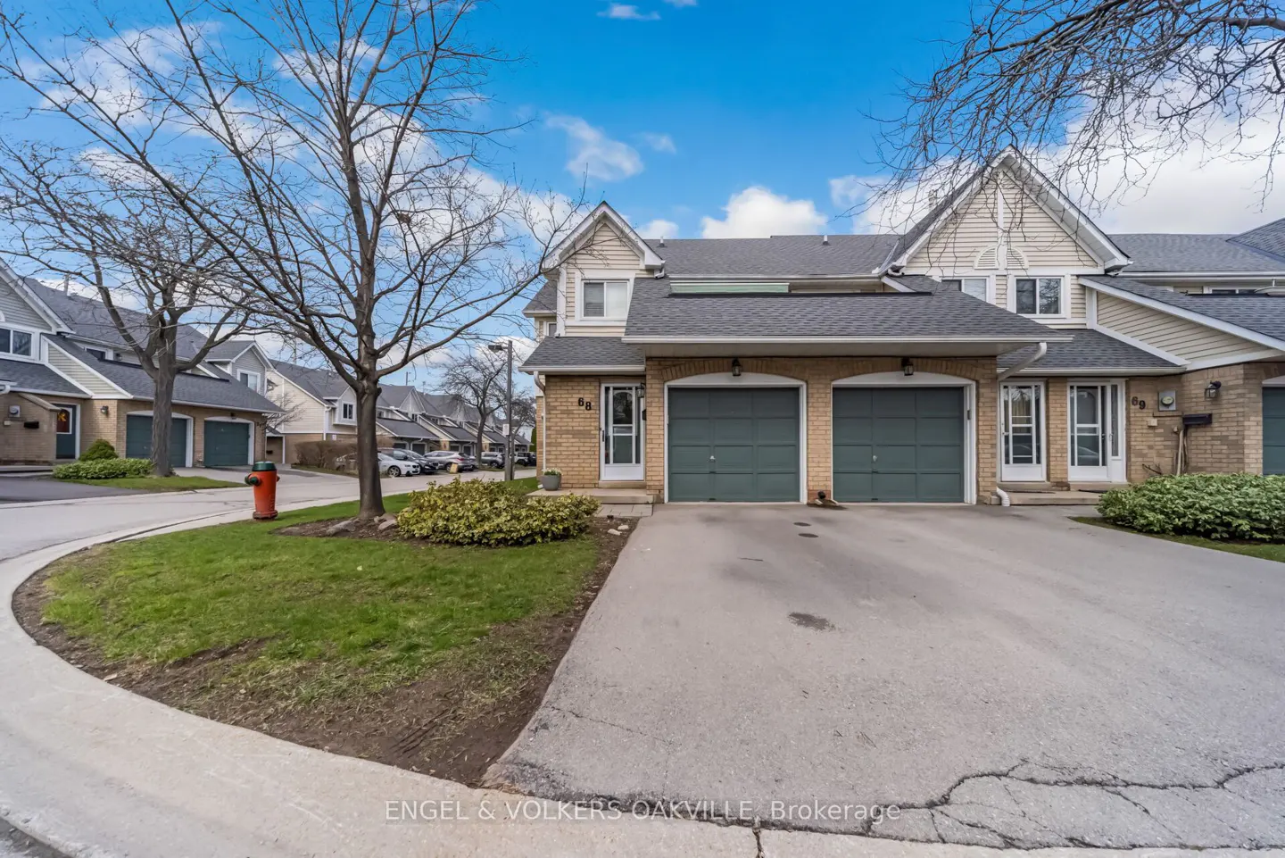 Exterior view of townhouses with green garage doors, brick facade, and a concrete driveway on a sunny day.