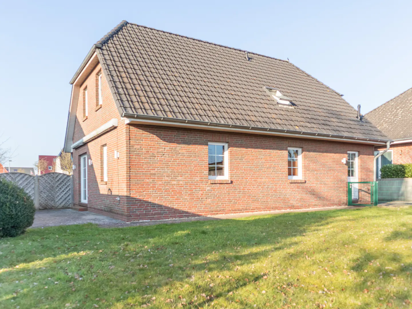 A red brick house with a gray tiled roof, white windows, and a green lawn.