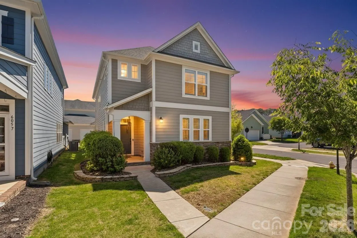 Two-story gray suburban home with a stone base, front porch, and manicured landscaping at sunset.