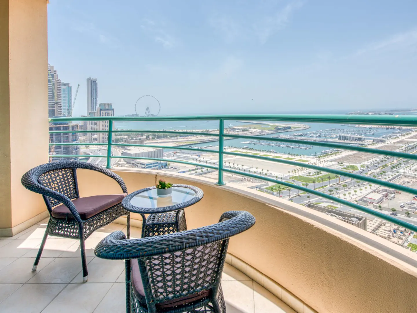 Balcony view with two wicker chairs, a glass table, and a city skyline with water in the background.
