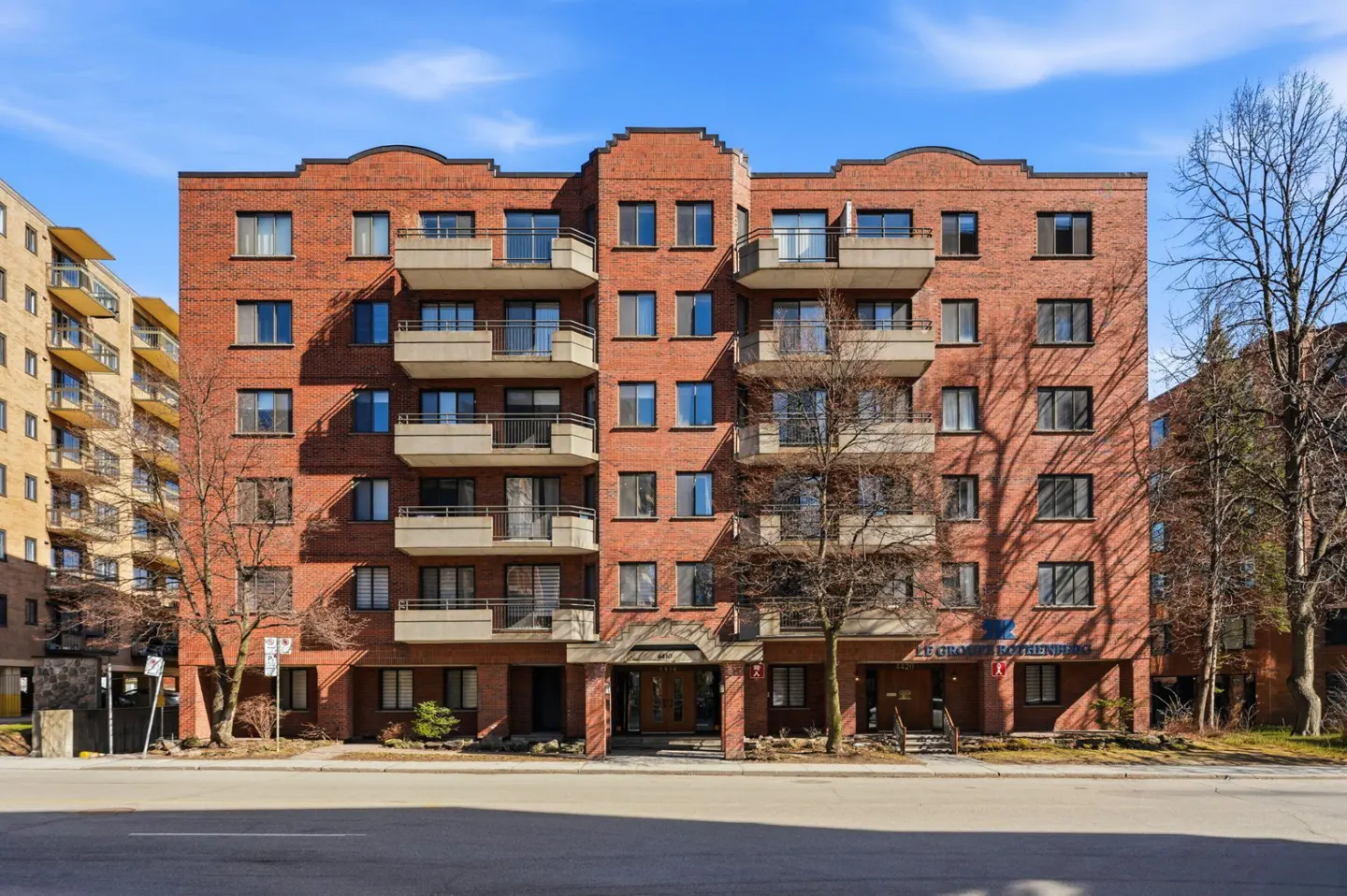 Exterior view of a red brick apartment building with balconies under a blue sky.
