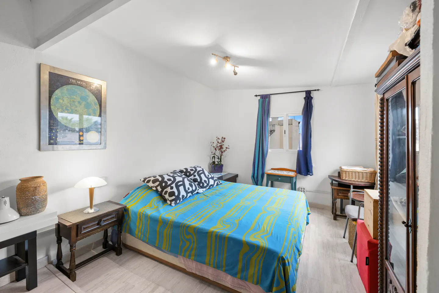 Bright bedroom with blue and yellow bedspread, black and white pillows, and a framed moon poster on the wall.