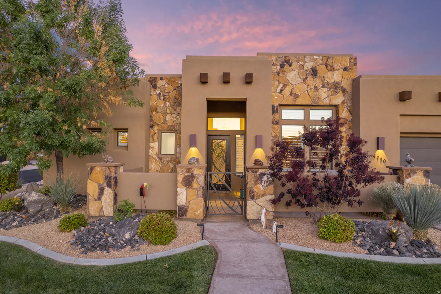 Tan stucco home with stone accents, a metal gate, and desert landscaping at dusk.