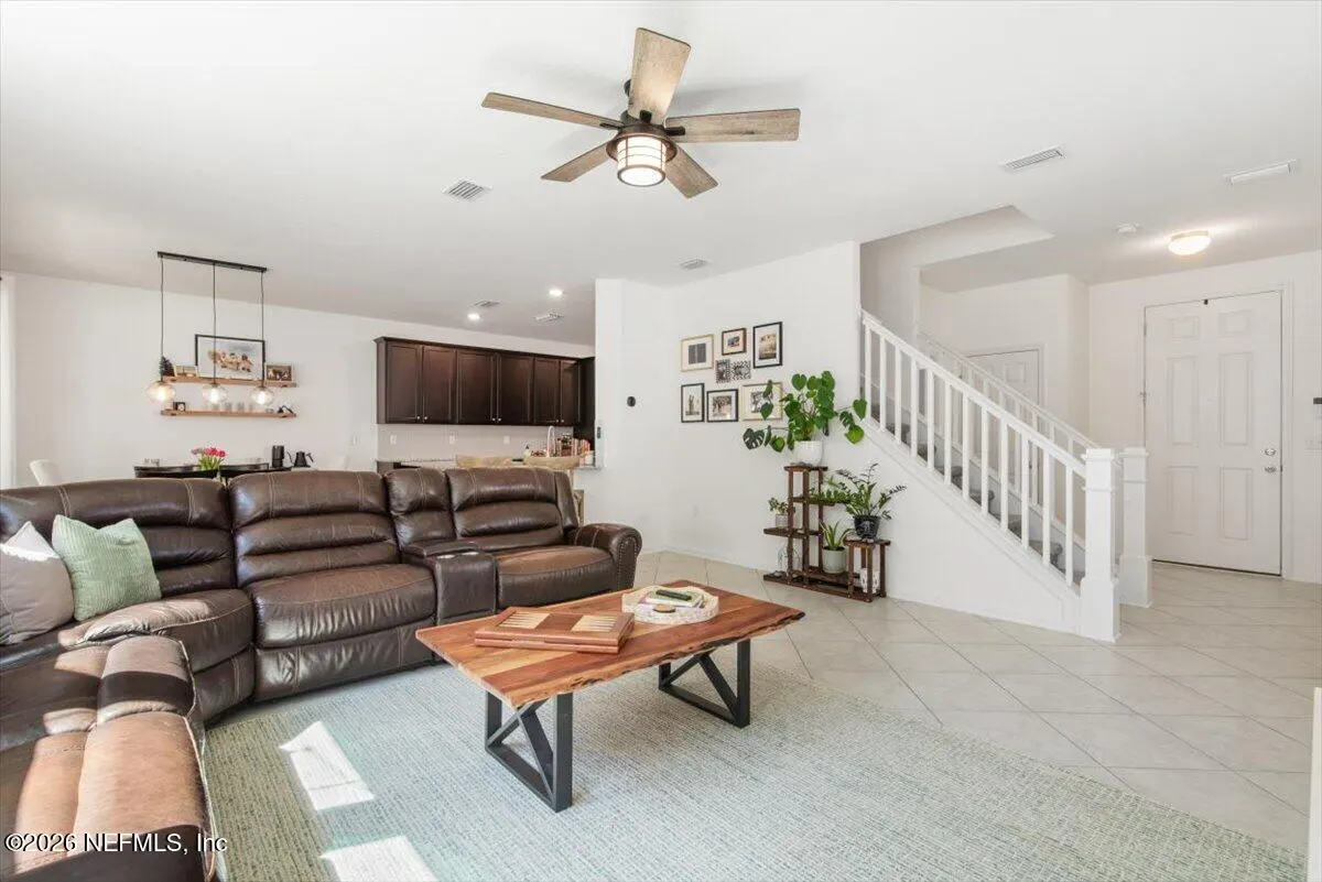 Bright living room with a brown leather sectional sofa, a wood coffee table, and a staircase with white railings.