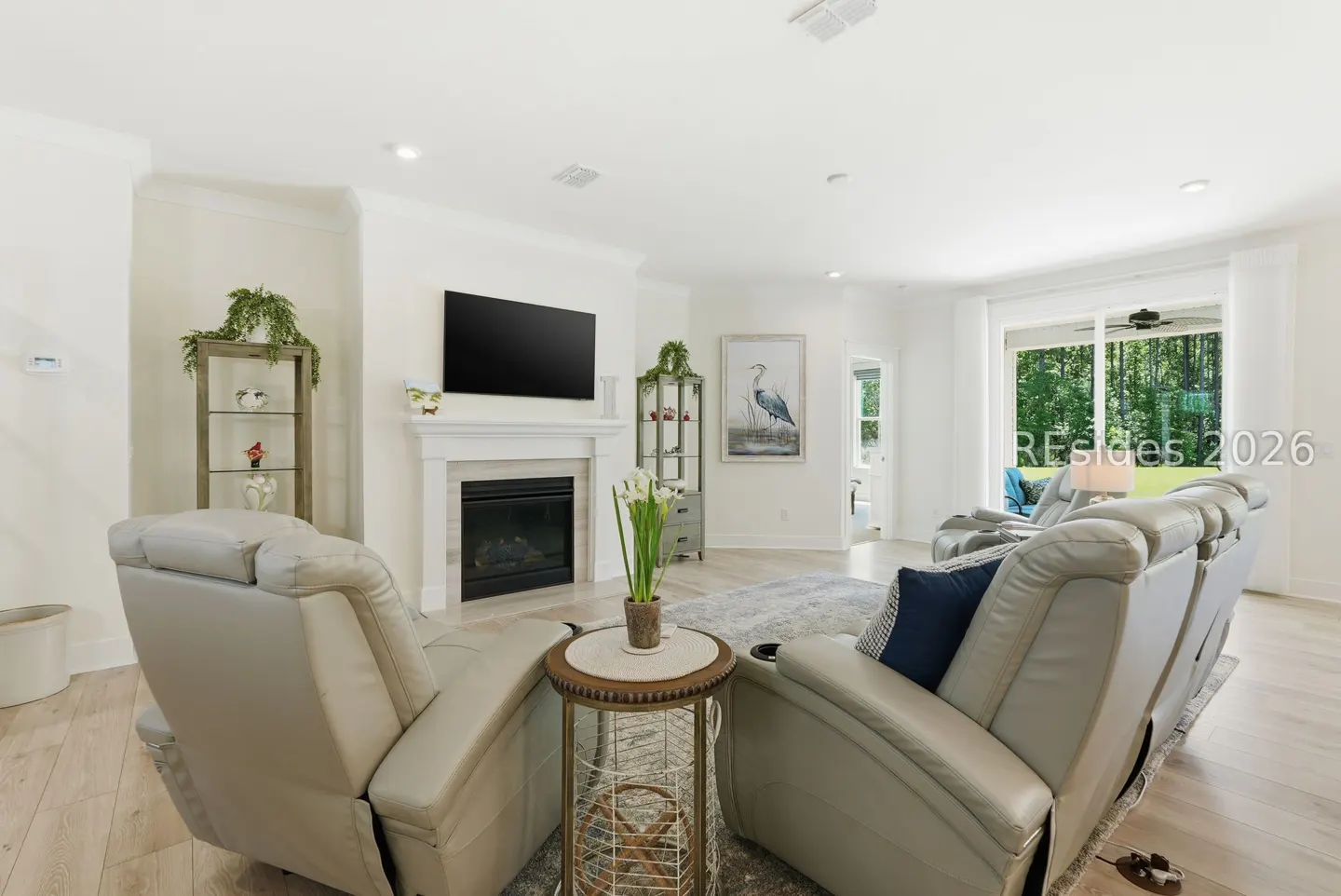 Bright living room with beige leather recliners, fireplace, and TV. A glass door leads to a green backyard.