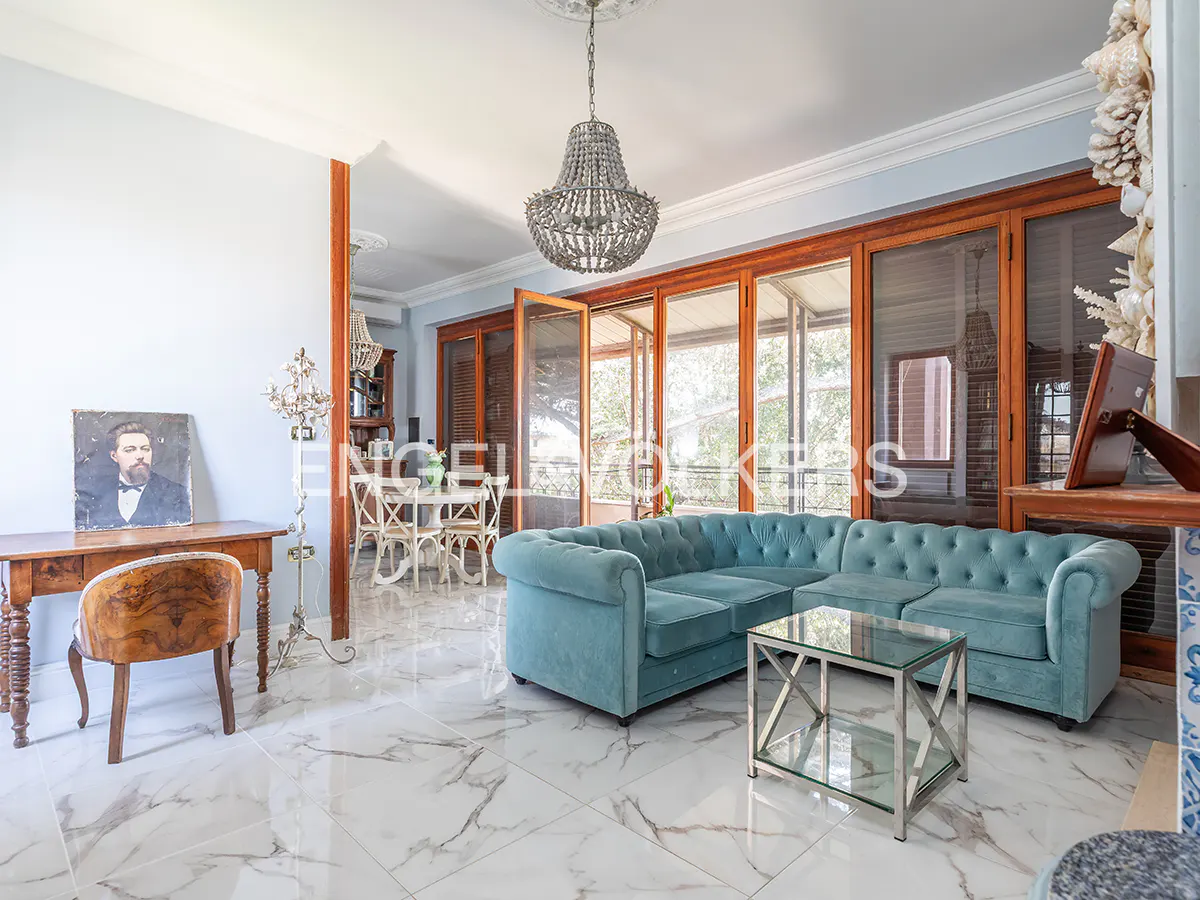 Living room with marble floors, a blue sectional sofa, and a glass coffee table. A chandelier hangs from the ceiling. French doors lead to a balcony.