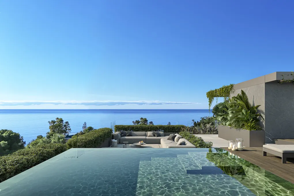 Luxury outdoor space with a pool overlooking the ocean. Gray sectional sofa, green plants, and clear blue sky.