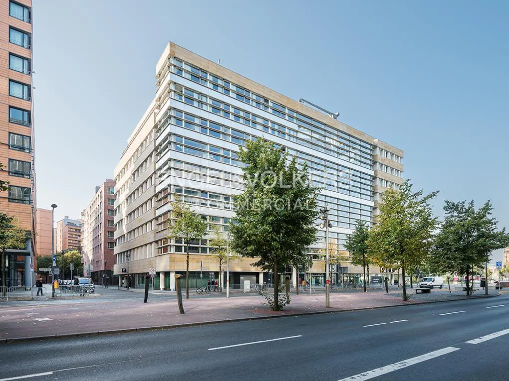 Exterior view of a modern, multi-story commercial building with glass windows and beige accents on a city street.