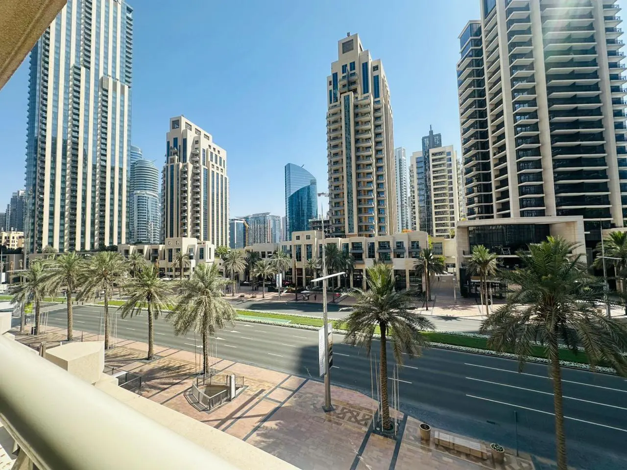 View from a balcony overlooking a Dubai street lined with palm trees and modern high-rise buildings under a clear blue sky.