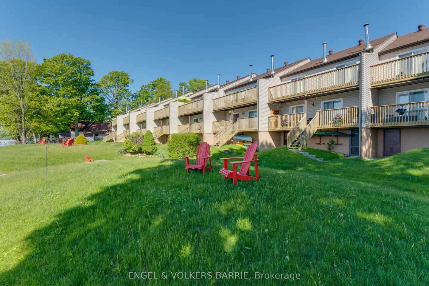 Row of townhouses with balconies and stairs to the lawn. Two red Adirondack chairs sit on the green grass. Blue sky.