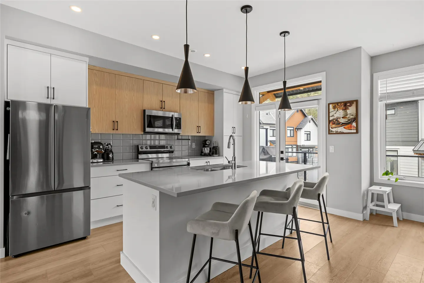 Bright kitchen with stainless steel appliances, white cabinets, and a gray island with three stools. Pendant lights hang above the island.
