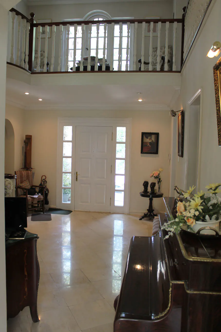 A bright foyer with marble floors, a white front door with sidelights, and a second-story balcony with white railings.