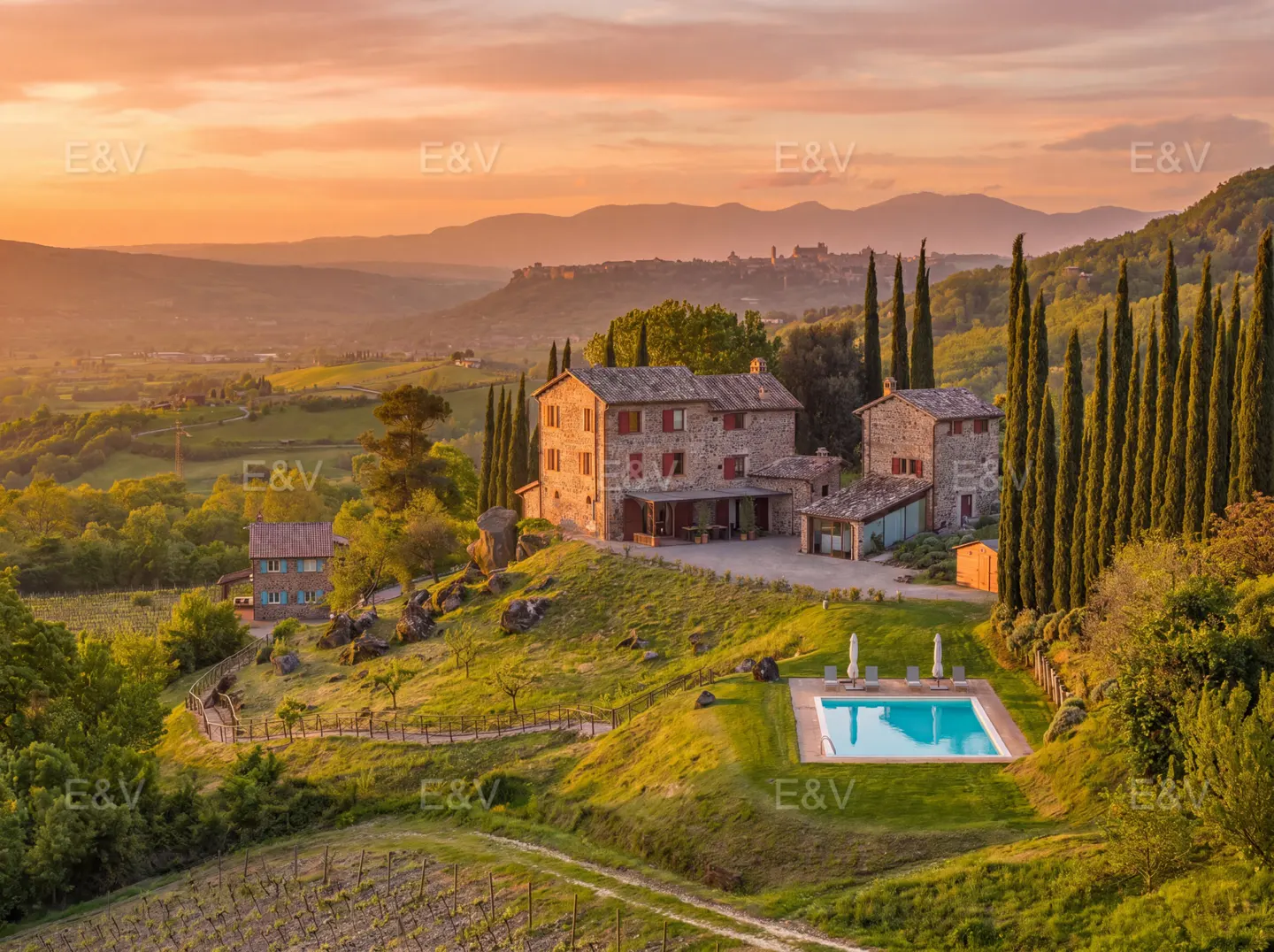 Tuscan villa with pool at sunset. Stone house with red shutters, cypress trees, and rolling hills in the background.