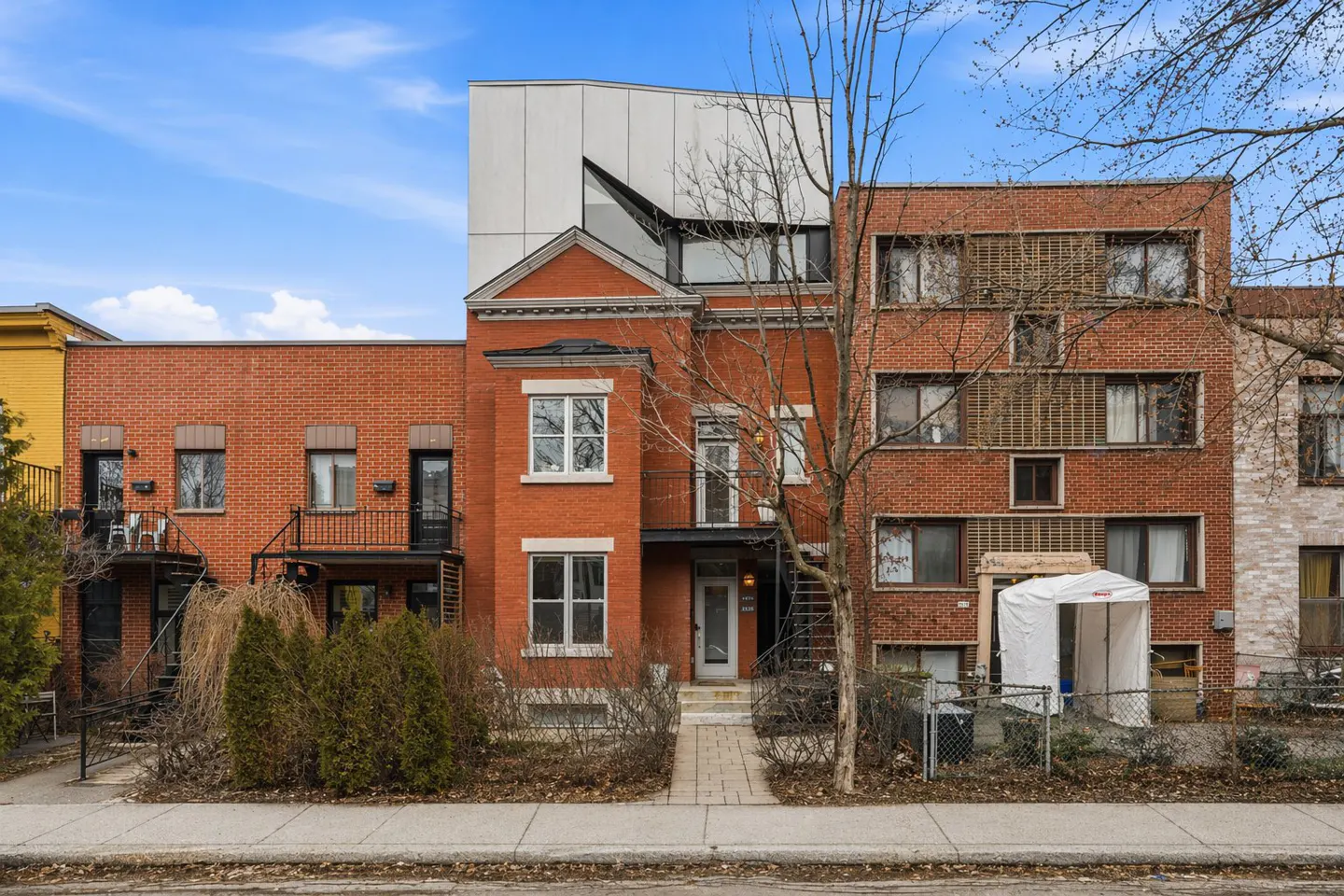 Row of brick townhouses with a modern white addition on the center building under a blue sky.