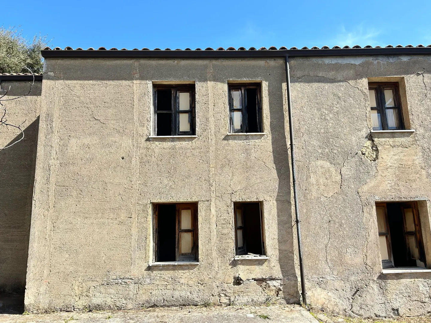 Exterior of a weathered, two-story building with six dark, open windows under a blue sky.