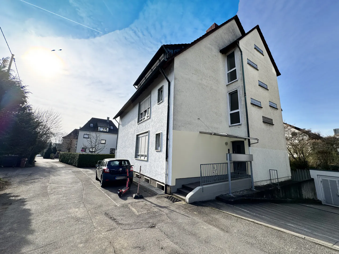 Exterior view of a three-story white building with a dark roof and a car parked in front.