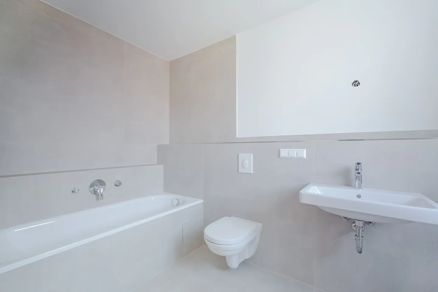 Bright bathroom with white tub, toilet, and sink against light gray walls. A chrome faucet is visible.