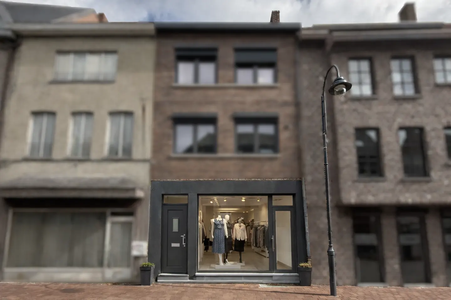 Storefront of a clothing boutique with mannequins in the window, set between brick buildings on a city street.