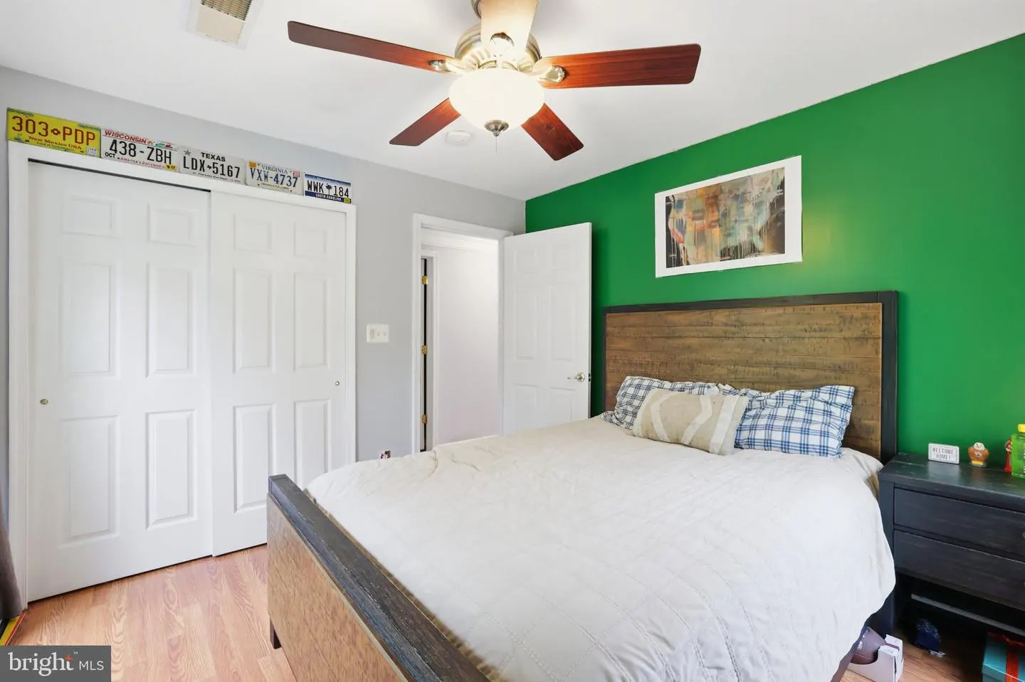 Bedroom with a bed, green accent wall, wood headboard, ceiling fan, and white closet doors with license plate decor.