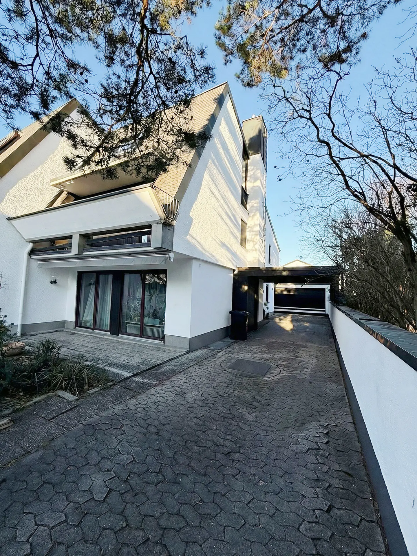 Exterior of a modern white house with a gray brick driveway and a covered garage.
