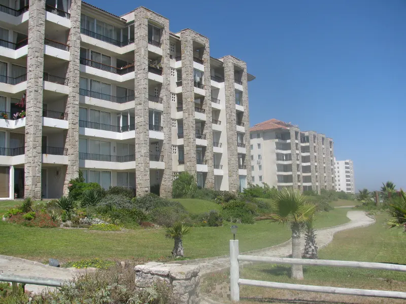 Exterior view of multi-story condo buildings with stone accents, balconies, and a green lawn with a winding path.