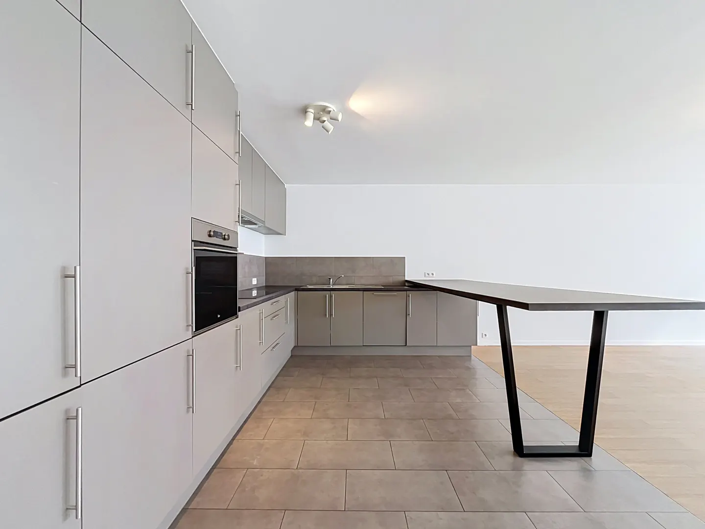 Modern kitchen with light gray cabinets, built-in oven, tiled floor, and a sleek breakfast bar with a black metal base.