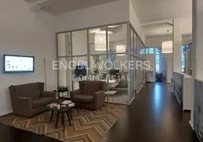 Office interior with brown sofas, a TV, and a glass-walled office area with Engel & Völkers Commercial logo.