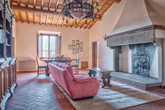 Living room with red brick floors, pink sofa, stone fireplace, wood table, and chandelier.