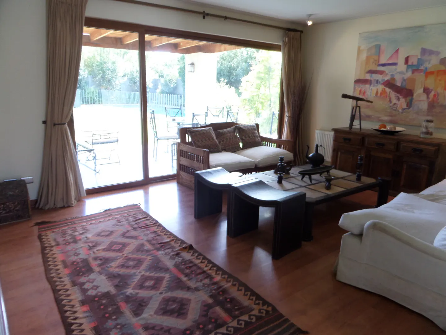 Living room with wood floors, a patterned rug, and a sliding glass door to a patio. A wooden sofa and coffee table are in the center.