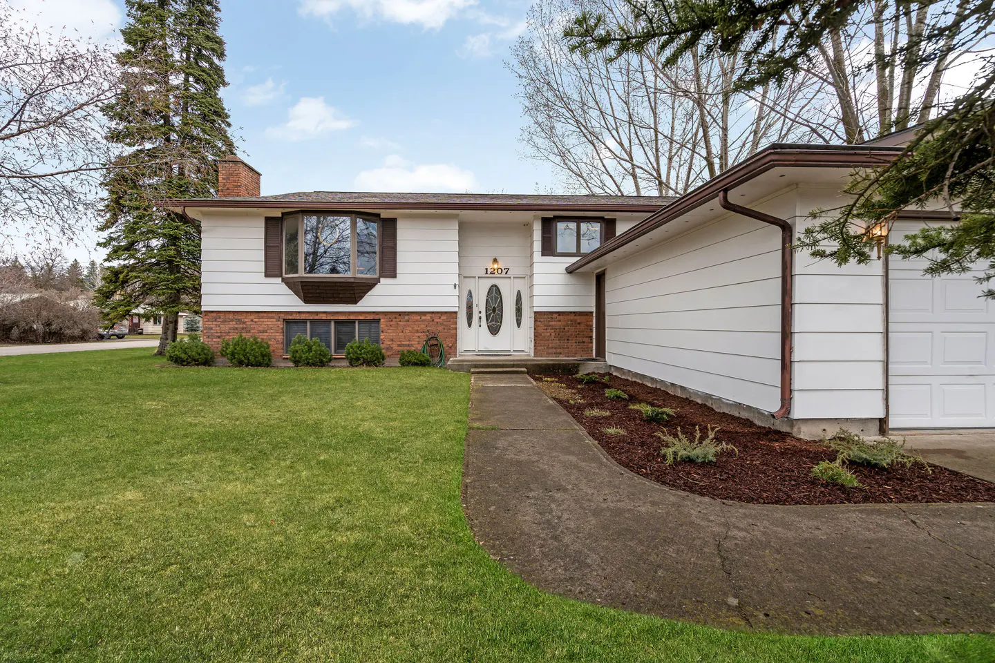Exterior shot of a two-story white house with a brick foundation, brown trim, and a green lawn. A concrete walkway leads to the front door.