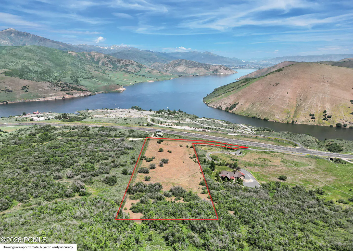 Aerial view of a vacant lot outlined in red, with a lake, mountains, and blue sky in the background.