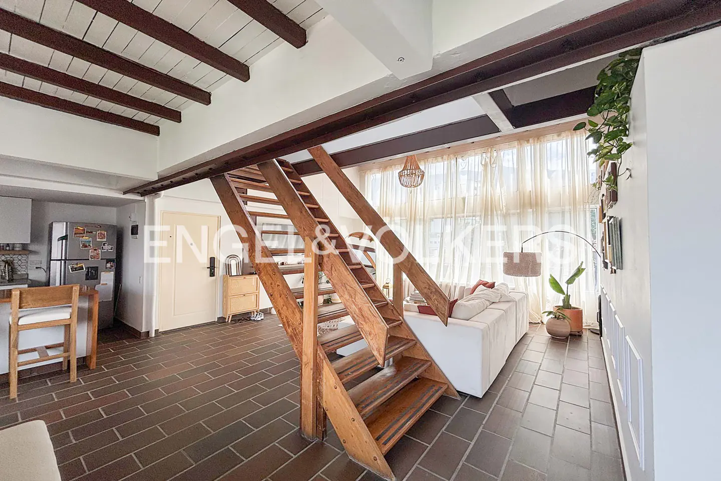 Interior view of a living space with wooden stairs, brick floors, and a white sofa near sheer curtains.