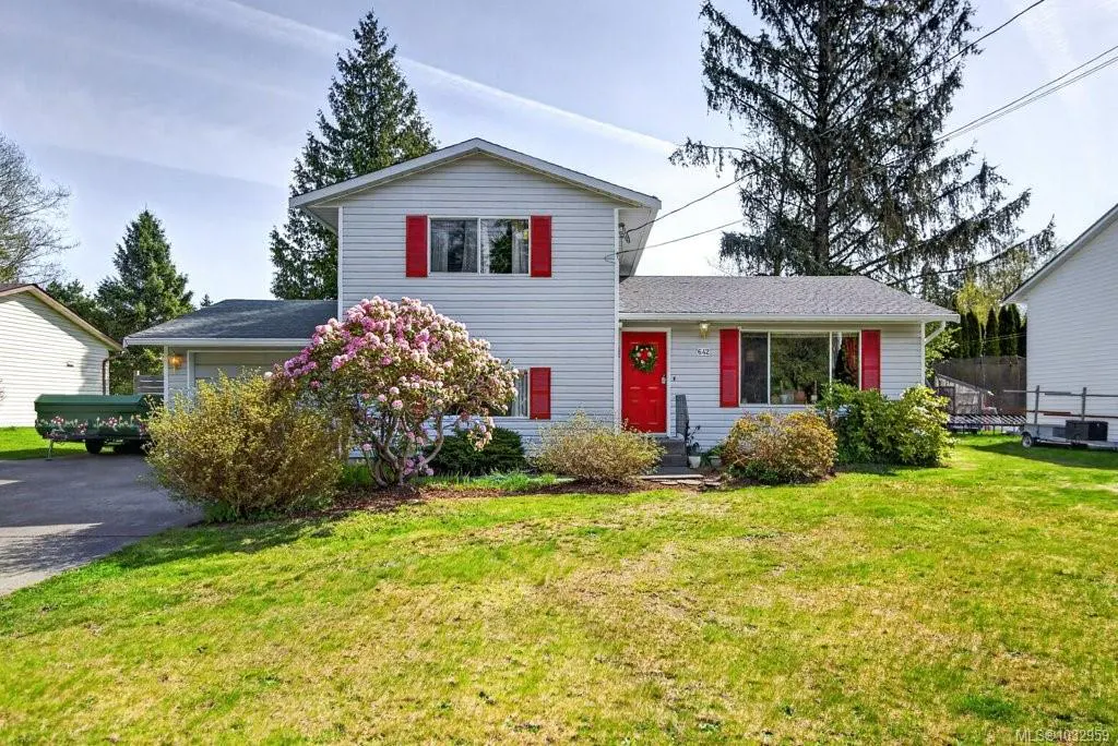 Two-story white house with red shutters and door, green lawn, and flowering bushes.