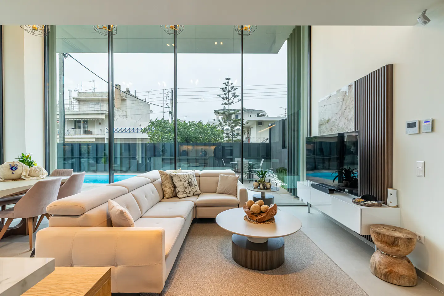 Living room with beige sectional sofa, round coffee table, and large windows overlooking a pool and backyard. TV and modern decor.