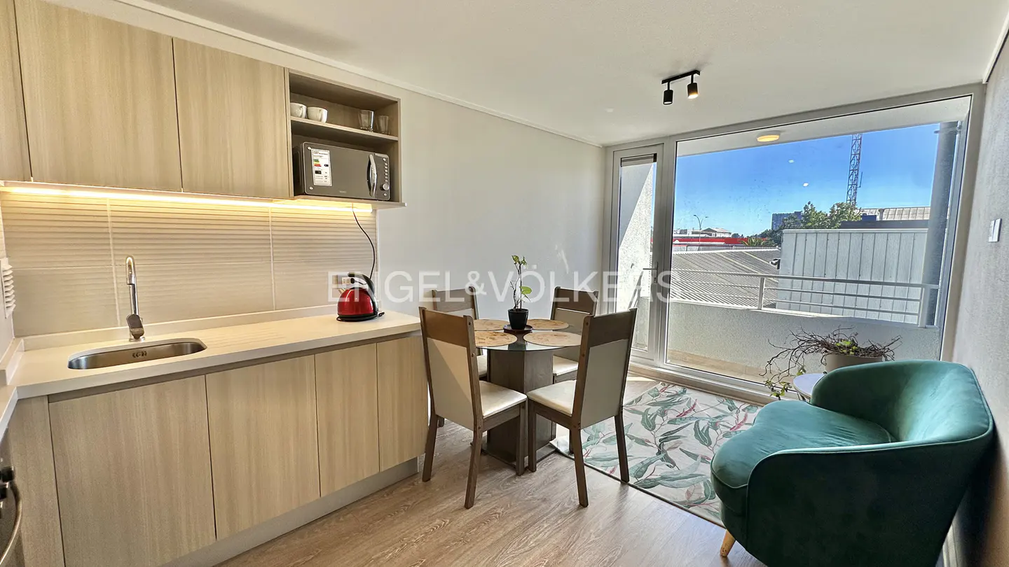 A bright apartment interior with a kitchen, dining table, and green armchair near a window.