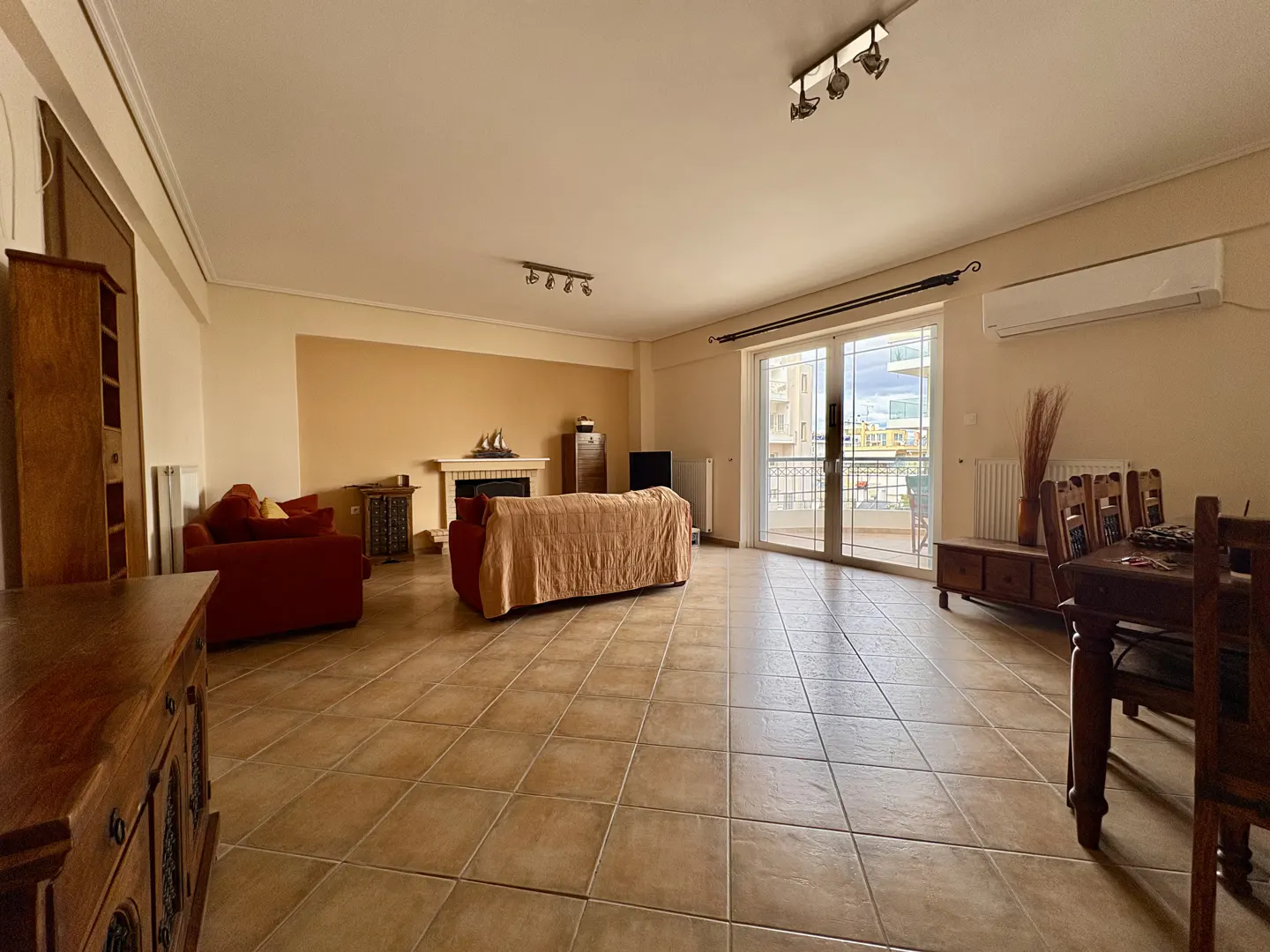 Spacious living room with tile floors, red sofas, fireplace, dining table, and sliding glass doors to a balcony.