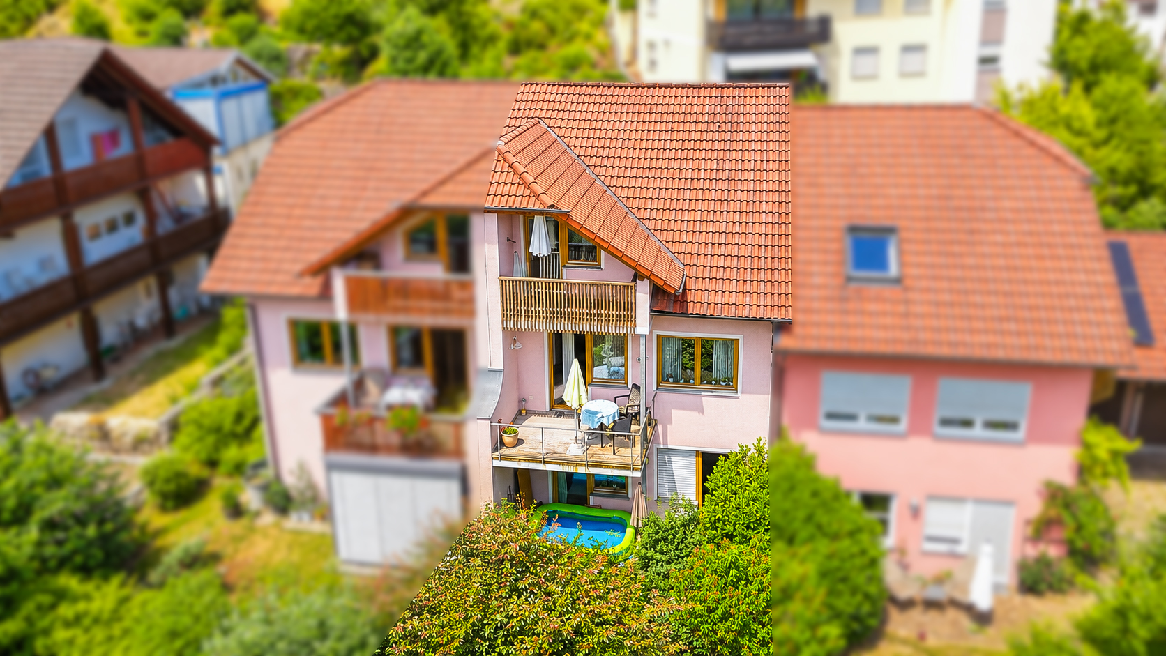 Aerial view of a pink house with a red tile roof, balconies, and a small inflatable pool in the garden.