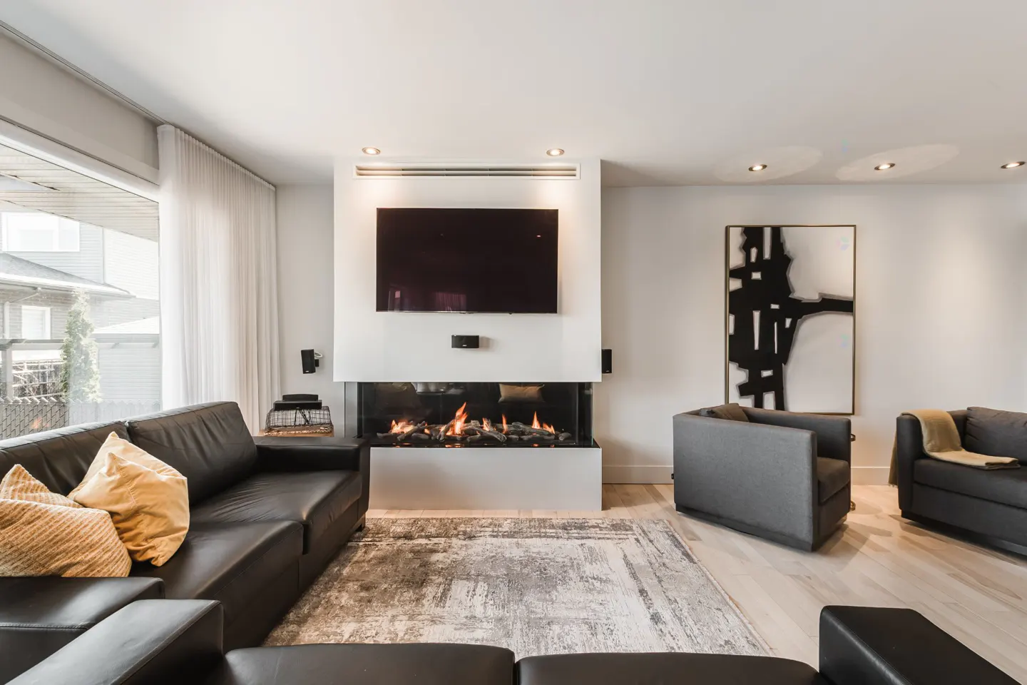Living room with a black leather sofa, gray chairs, and a modern fireplace with a TV above it.