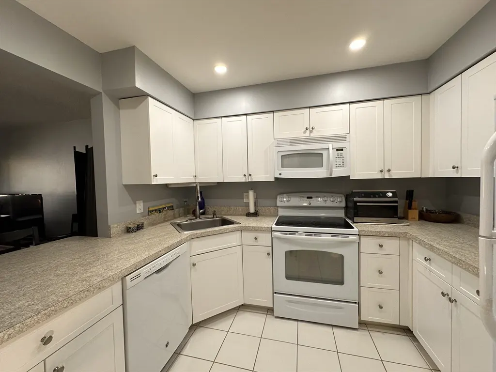 Bright kitchen with white cabinets, appliances, and tile floor. Granite countertops and gray walls.