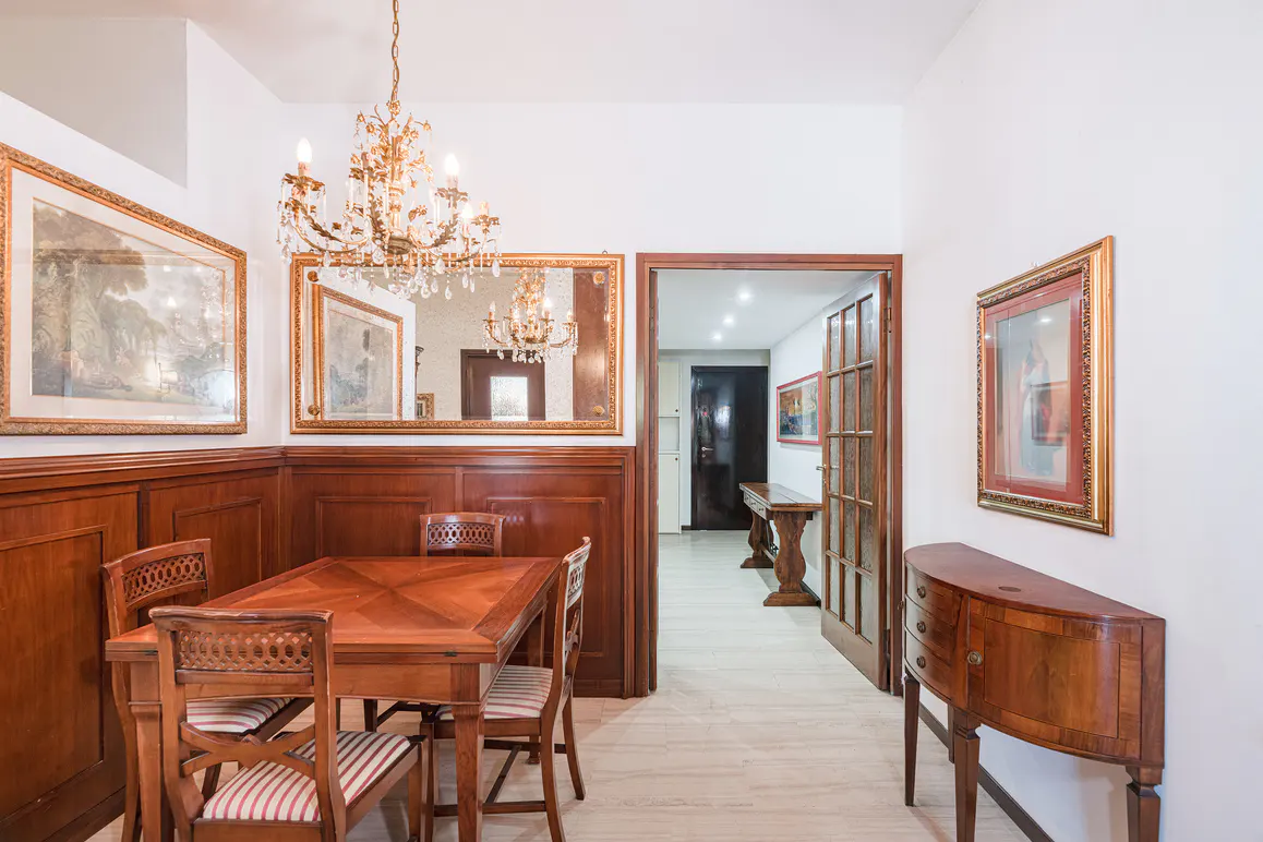 A dining room with wood paneling, a table with chairs, and a chandelier. A hallway is visible through a doorway.