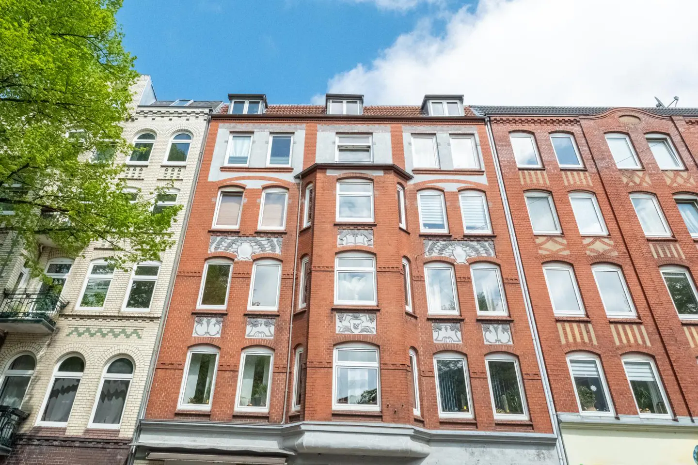 Low-angle view of a red brick apartment building with white-framed windows and decorative stone accents under a blue sky.