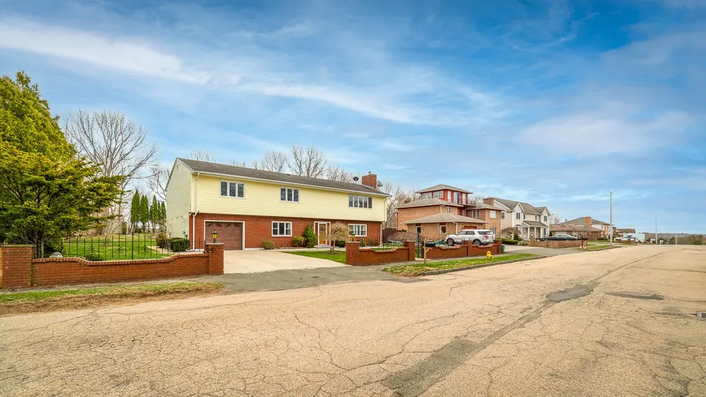 Two-story yellow house with a brick base and garage, set back from the street with a brick wall and iron fence.