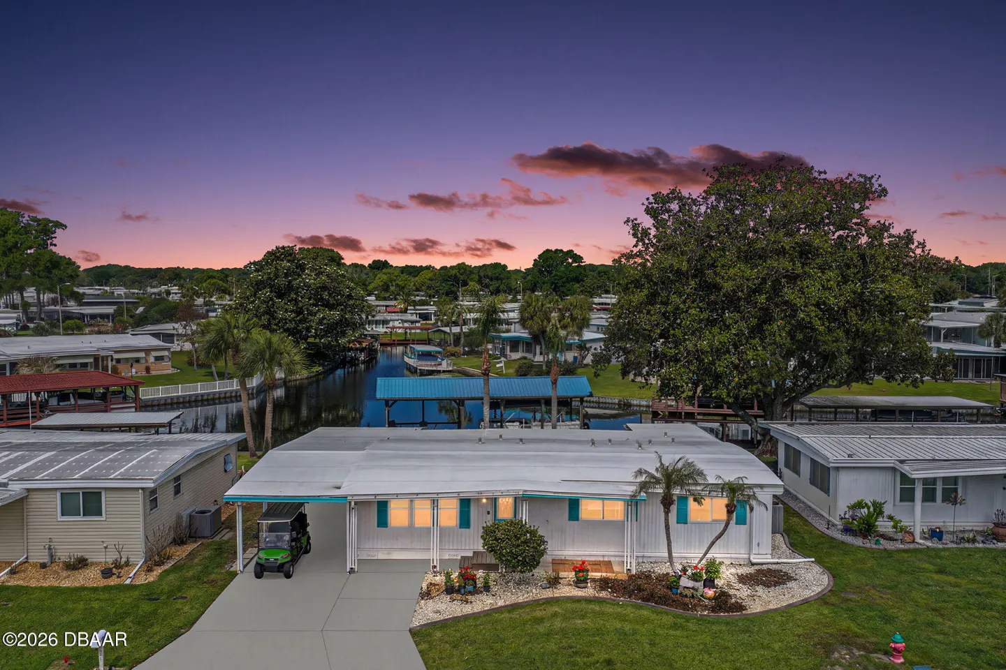 Aerial view of a white single-story home with turquoise shutters and a green golf cart in the driveway. A canal runs behind the house.