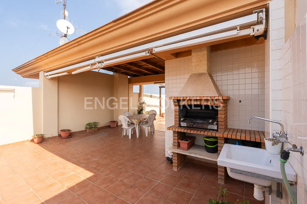 Outdoor patio with a brick barbecue, sink, and dining table under a covered area with a tiled floor.